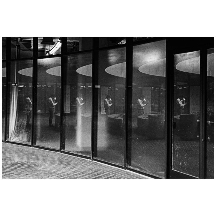 A man is visible through a series of large windows, with his reflection repeated multiple times.