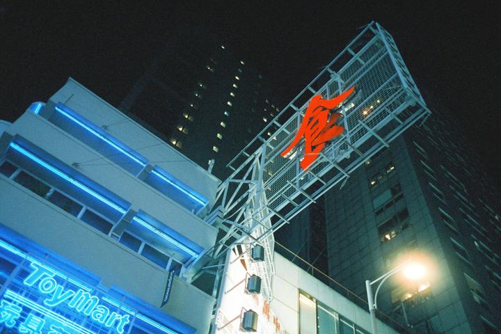 A low-angle view shows a building with blue neon lights and a large red sign against a dark night sky.