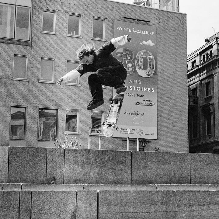 A man on a skateboard jumps in front of a building with a large banner.