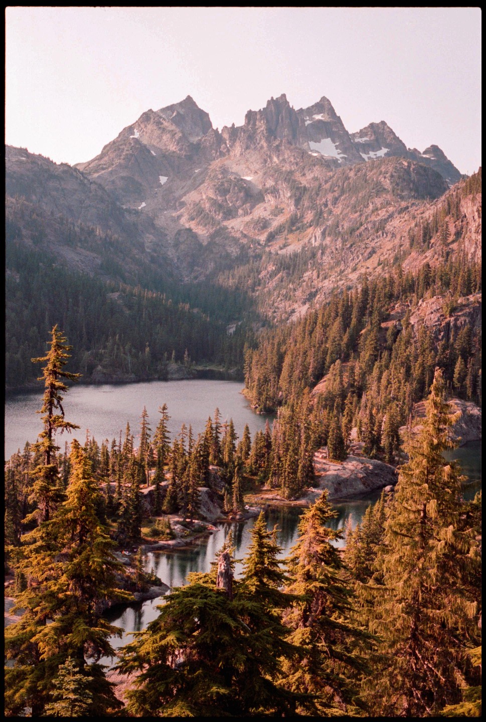 A lake surrounded by a dense forest of pine trees is nestled at the base of a rugged mountain range.