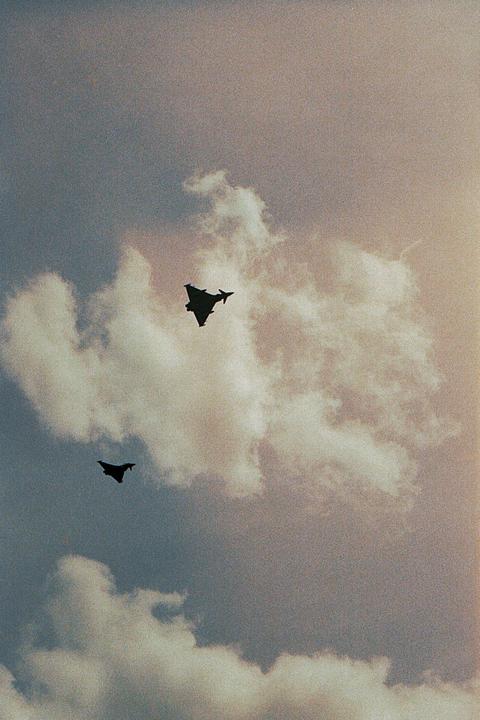 Two fighter jets are silhouetted against a cloudy sky.