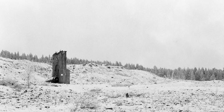 A tall, ruined concrete structure stands in a barren, snow-covered landscape with a forest in the background.
