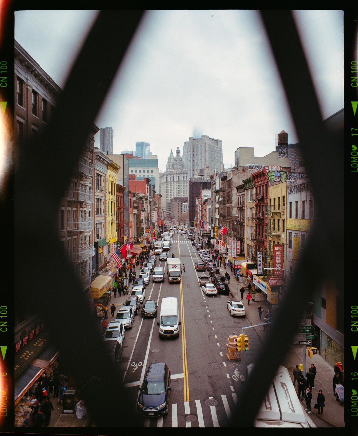 A street in Chinatown is filled with cars and pedestrians, framed by a dark, geometric shape.