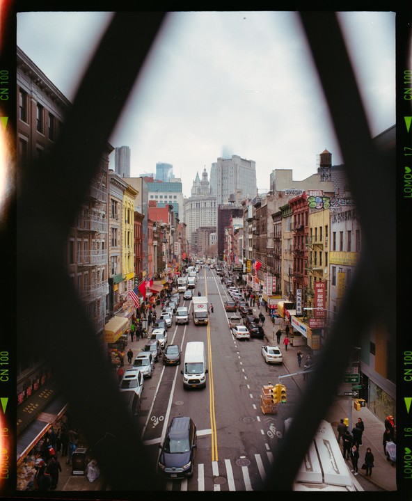 A street in Chinatown is filled with cars and pedestrians, framed by a dark, geometric shape.