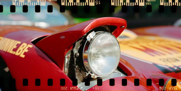 A close-up view of the headlight of a red sports car with yellow lettering on the hood.