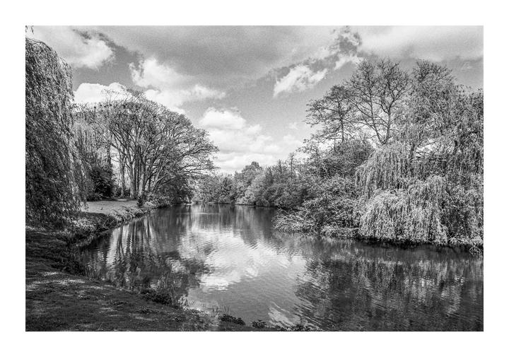 A river flows between banks covered in trees and grass under a cloudy sky.