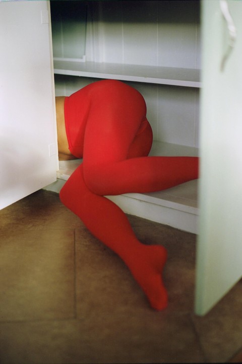 A person wearing red tights is bent over inside a white cabinet.