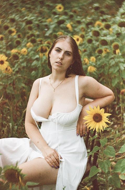 A woman in a white dress sits in a field of sunflowers.