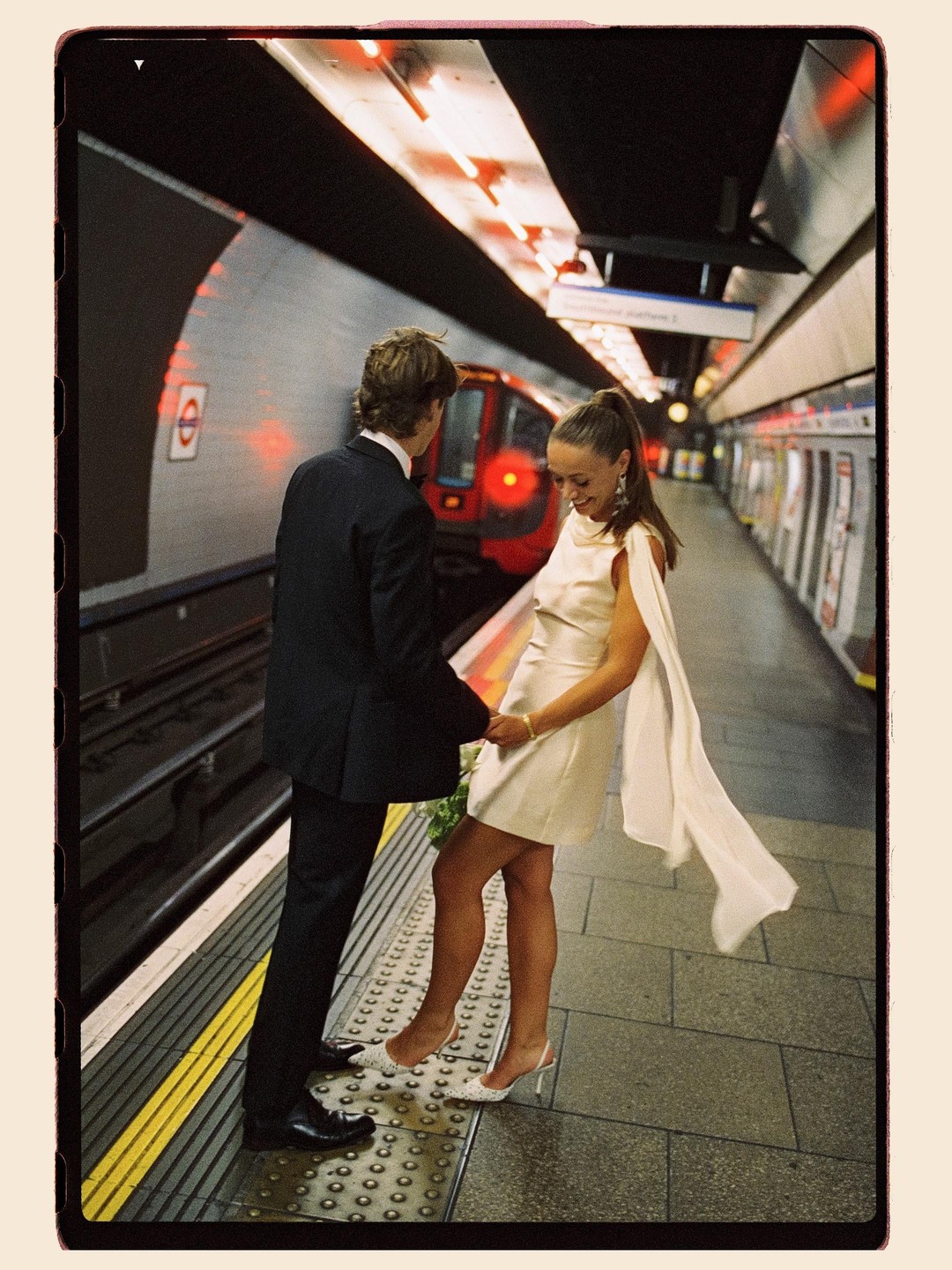 A couple stands on a subway platform as a train approaches.