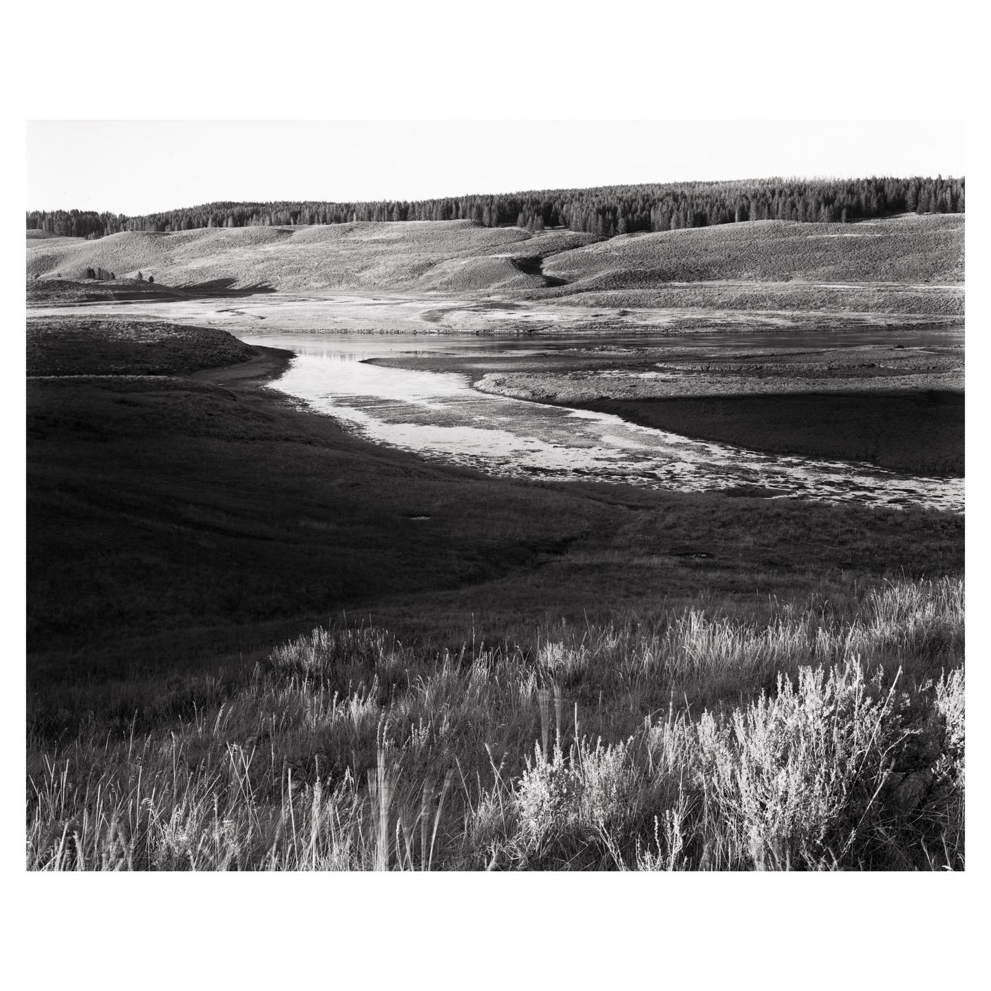 A winding river flows through a valley with hills covered in trees and grass.