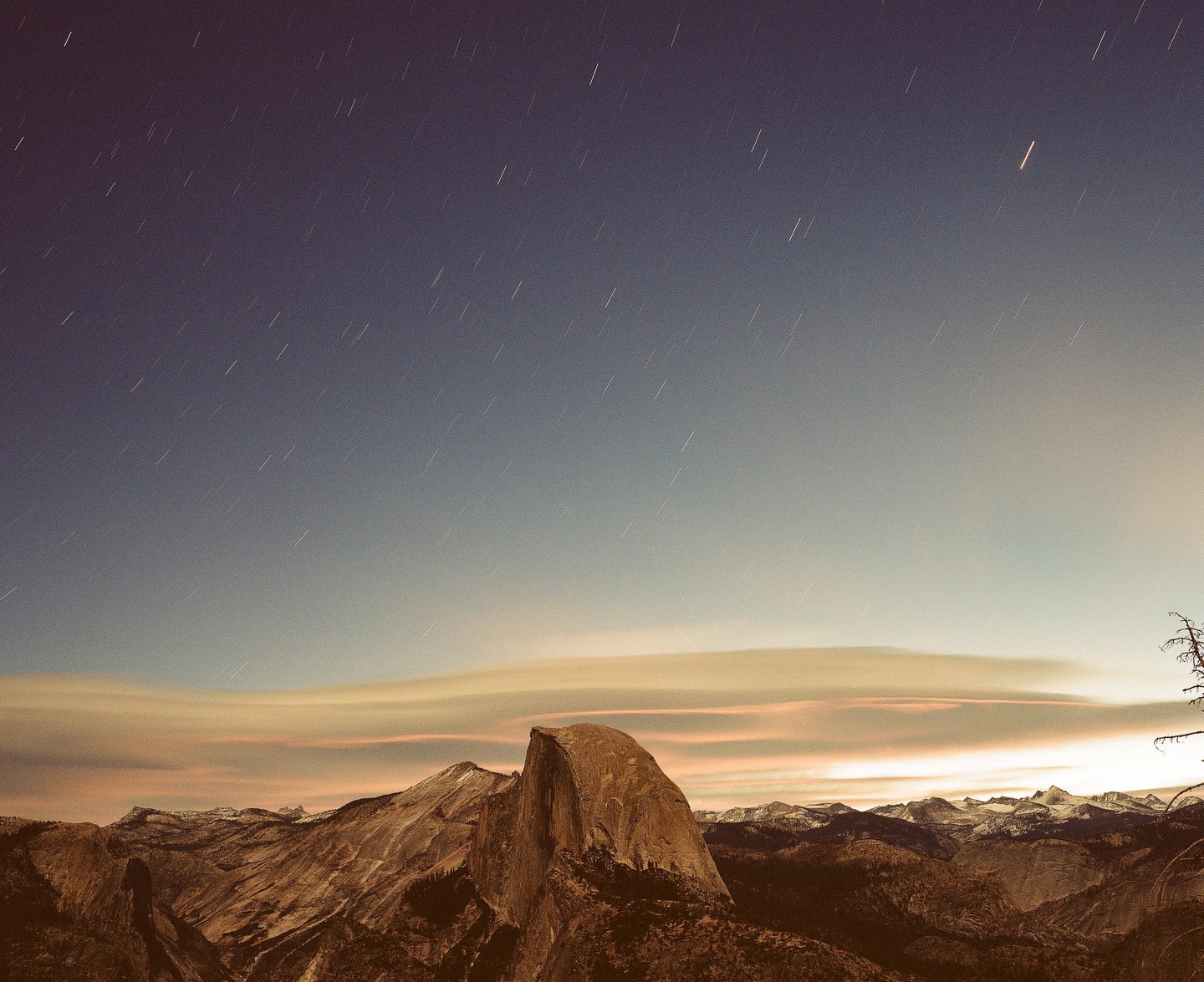 A mountain range with a prominent rock formation is visible under a night sky with star trails.