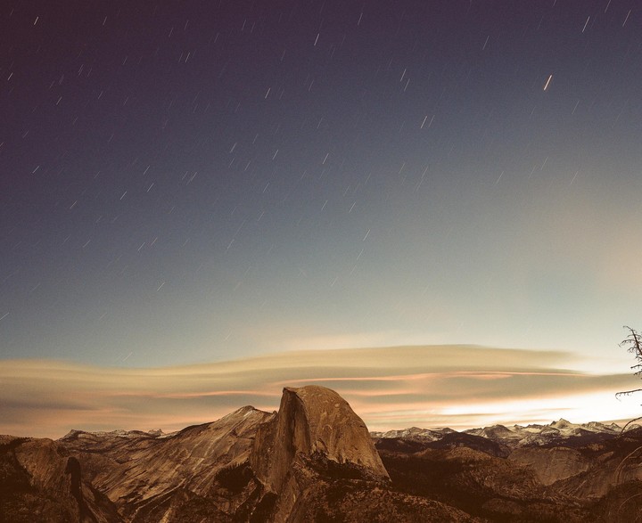 A mountain range with a prominent rock formation is visible under a night sky with star trails.