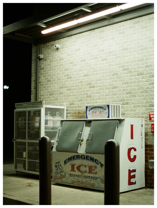 An ice vending machine and propane tank exchange are visible under fluorescent lights at night.