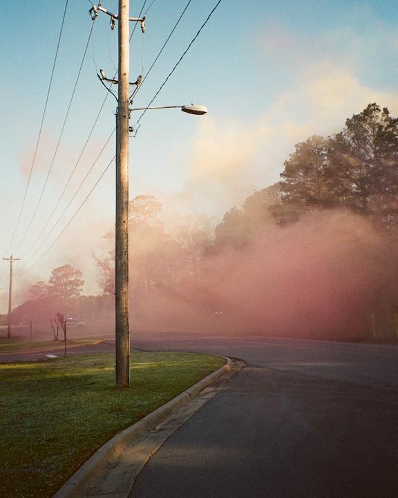 Pink smoke billows across a street with a utility pole and power lines.