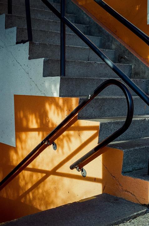A concrete staircase with black railings is painted white and orange, with shadows cast on the orange wall.