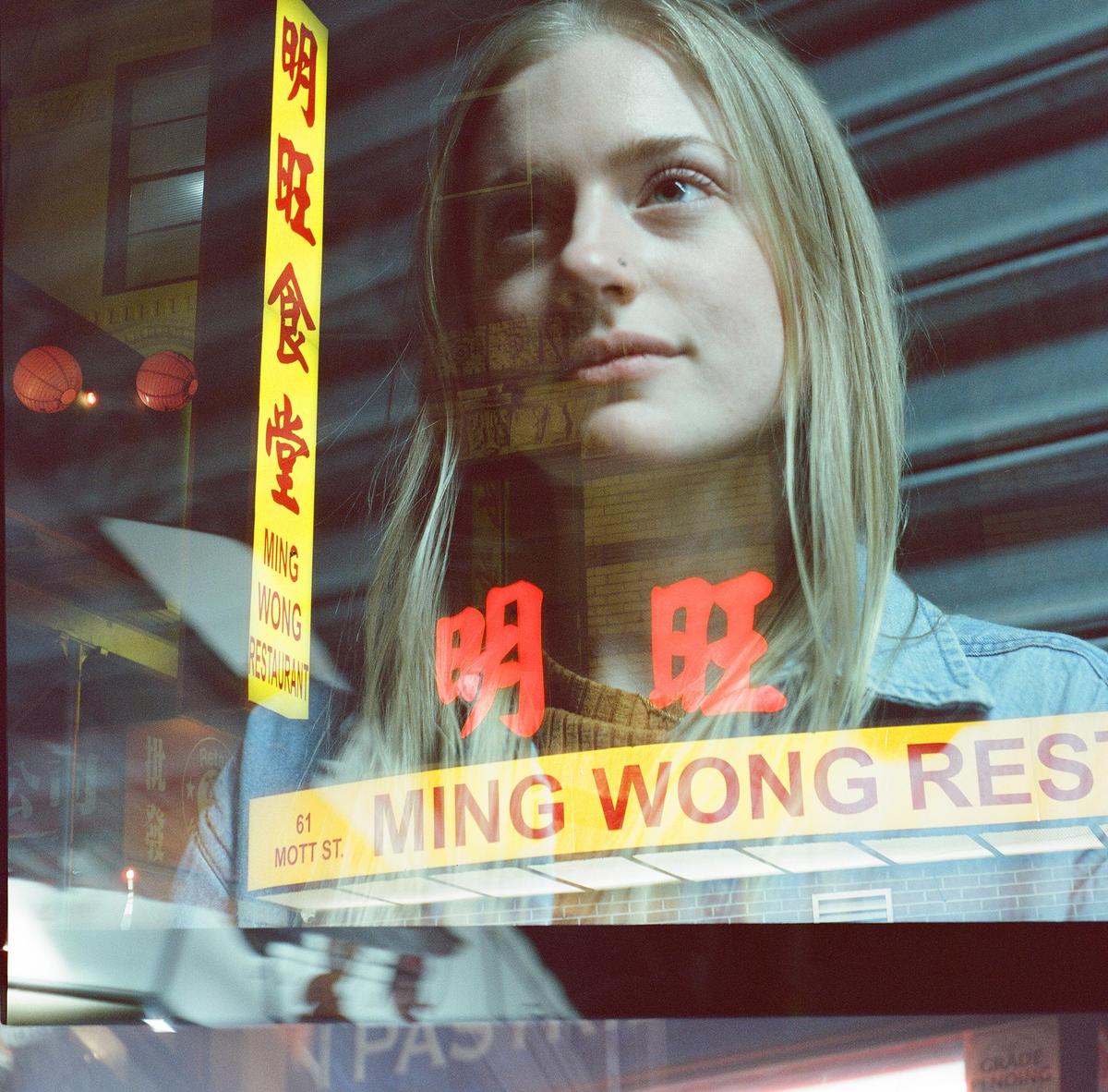 A woman is visible through a window with reflections of Chinese characters and restaurant signs.