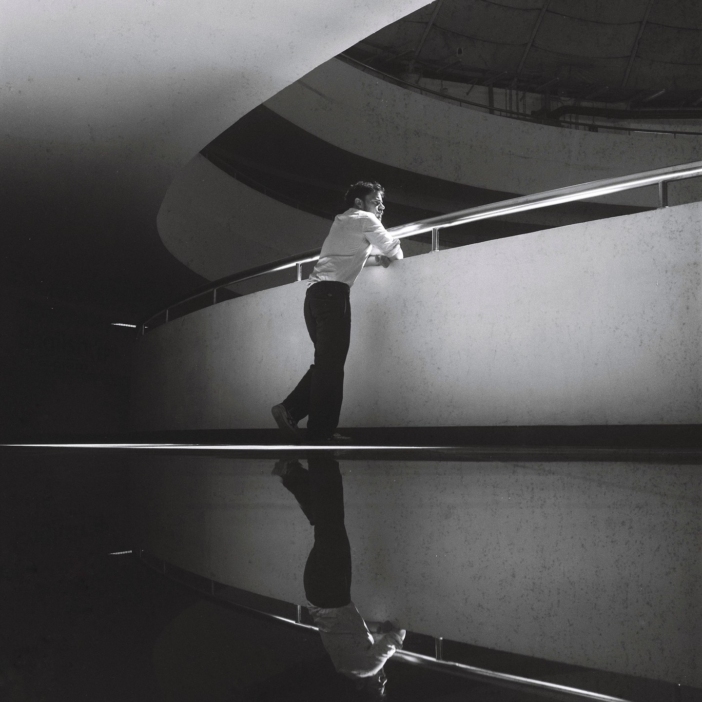 A man leans on a railing with his reflection visible below him.