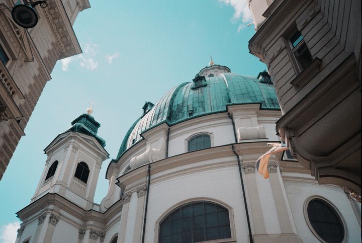A low-angle view shows a white church with a green dome and steeple against a bright blue sky.