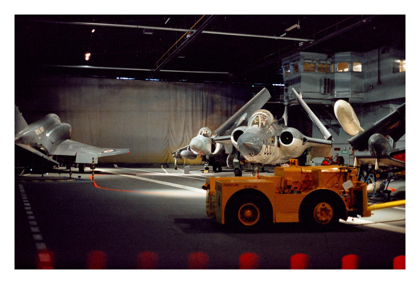 Three military aircraft and a yellow tow vehicle are parked inside a hangar.