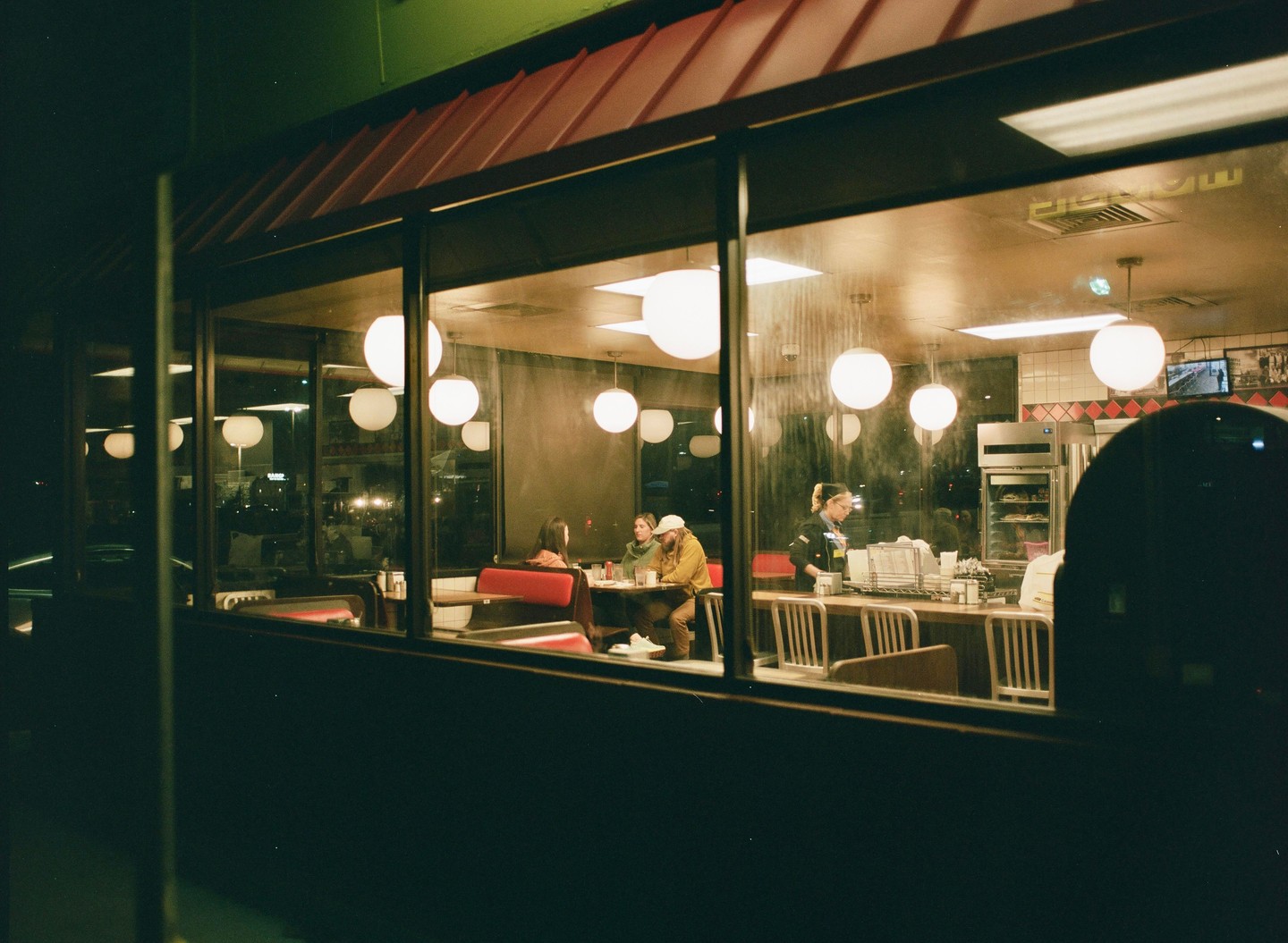 A group of people are visible through the window of a diner at night.