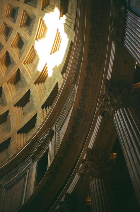 Light streams through the oculus of a coffered dome, illuminating architectural details and columns.