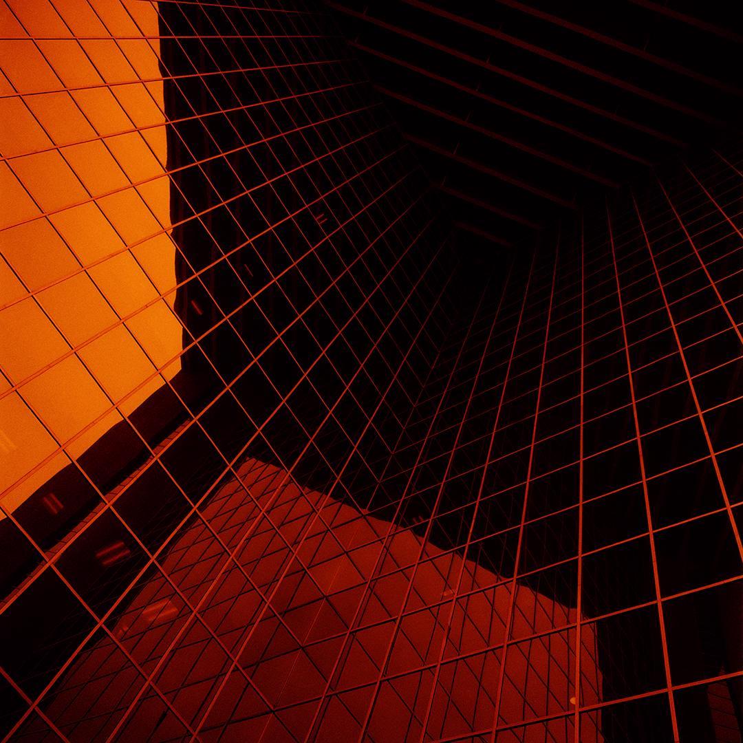 A low-angle view of a modern building with a grid pattern on its facade, reflecting an orange hue.