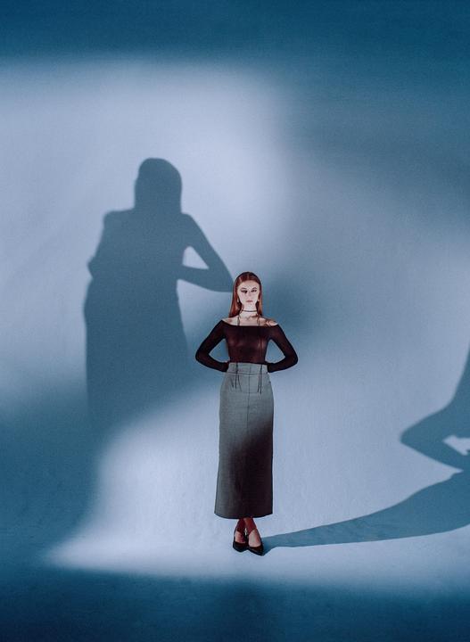 A woman stands with her hands on her hips, casting a large shadow on a blue wall.