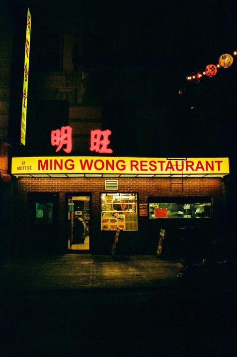 A brightly lit restaurant sign with Chinese characters and the name "Ming Wong Restaurant" is visible at night.