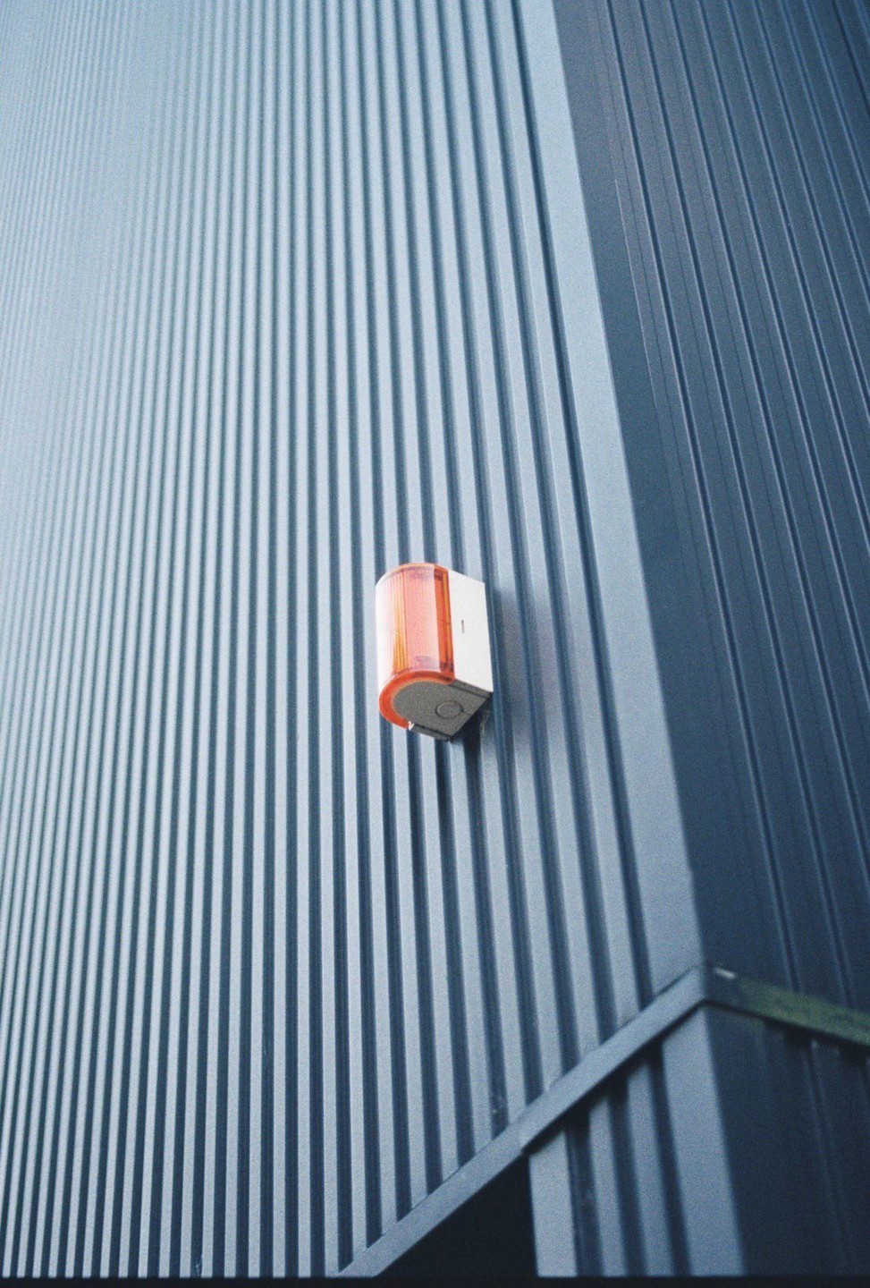An orange light is mounted on a corrugated metal wall.