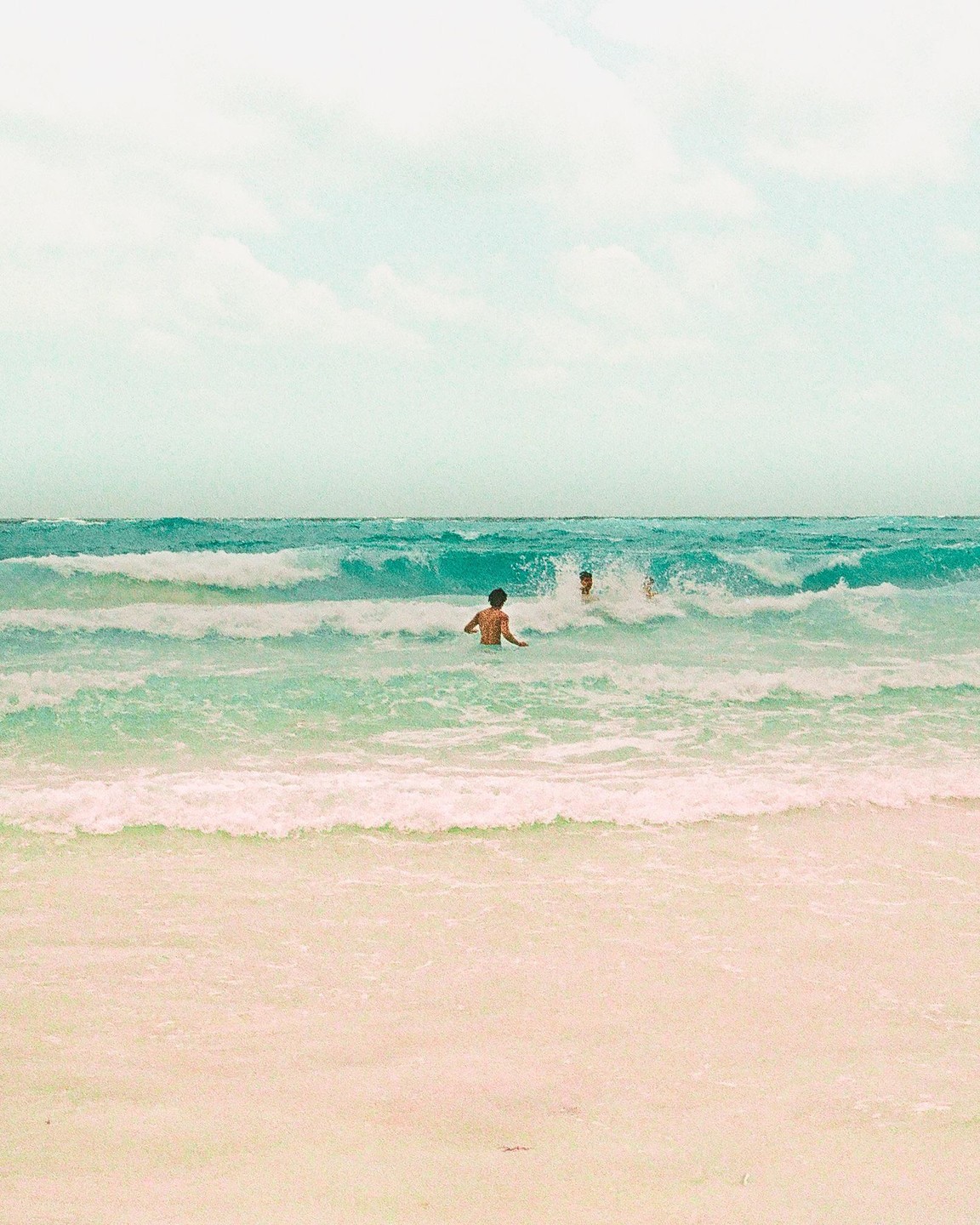Two men are in the ocean with waves crashing around them.