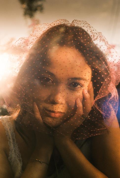 A woman with her hands on her face looks through a pink polka dot veil.