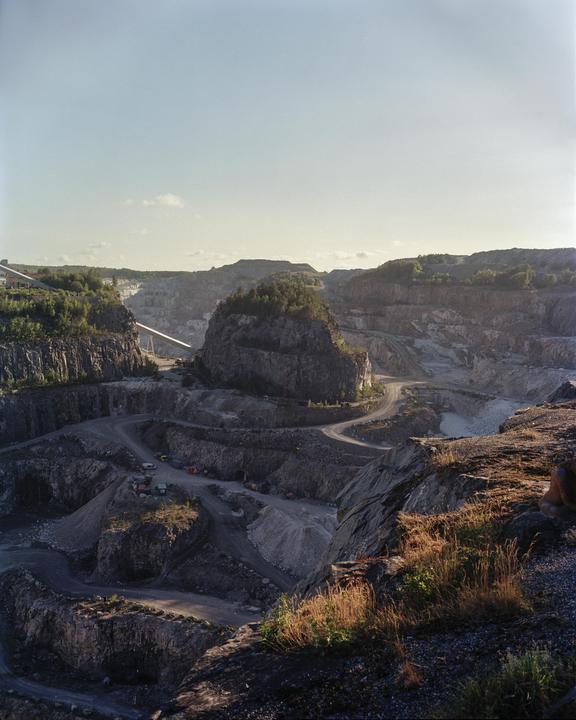A large limestone mine with winding roads and heavy machinery is visible under a clear sky.