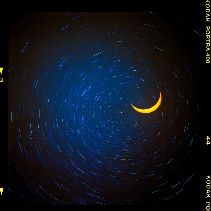 A crescent sun is visible against a dark sky with circular star trails.