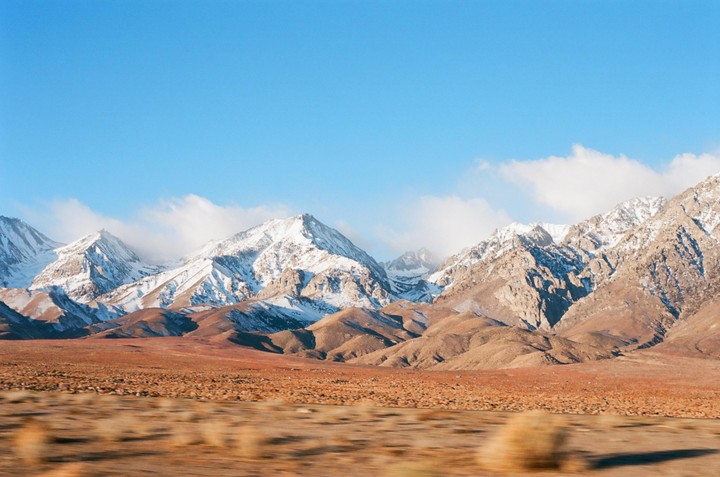 Snow-capped mountains rise above a vast, arid landscape under a clear blue sky.