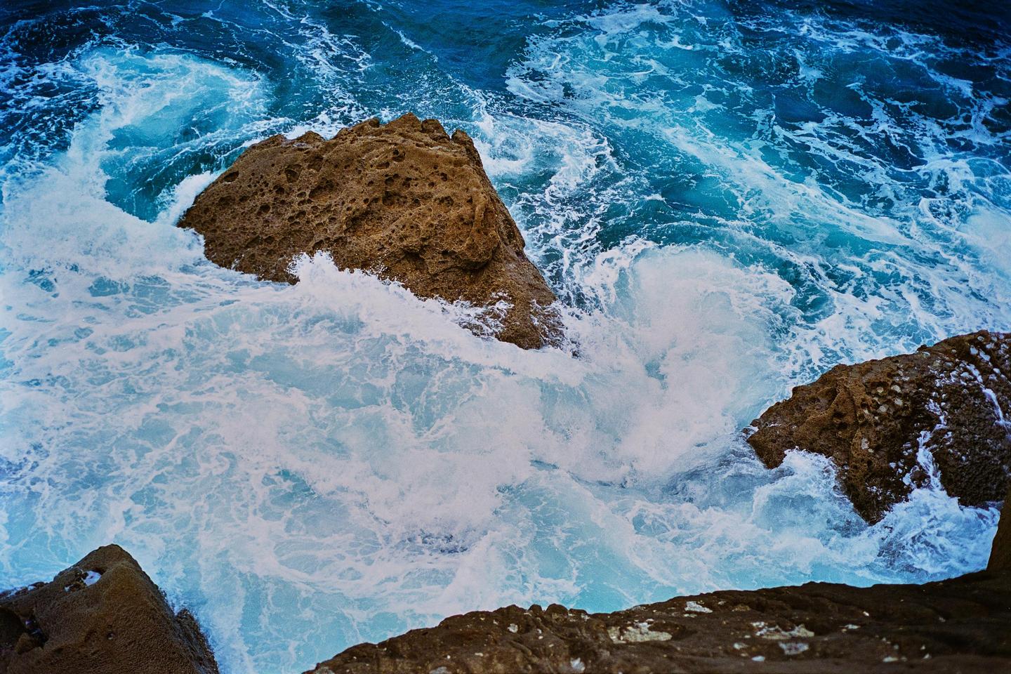 Waves crash against a rocky shore, creating white foam against the blue ocean.