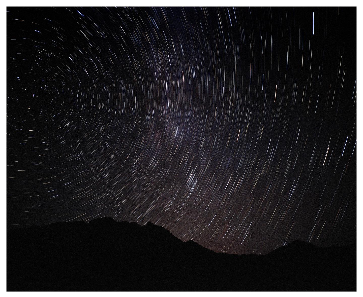 Star trails arc across the night sky above a dark mountain range.