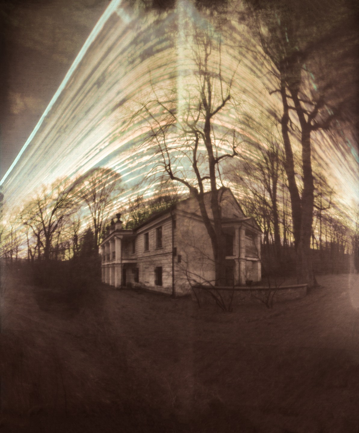 An abandoned mansion stands among bare trees under a streaked sky.