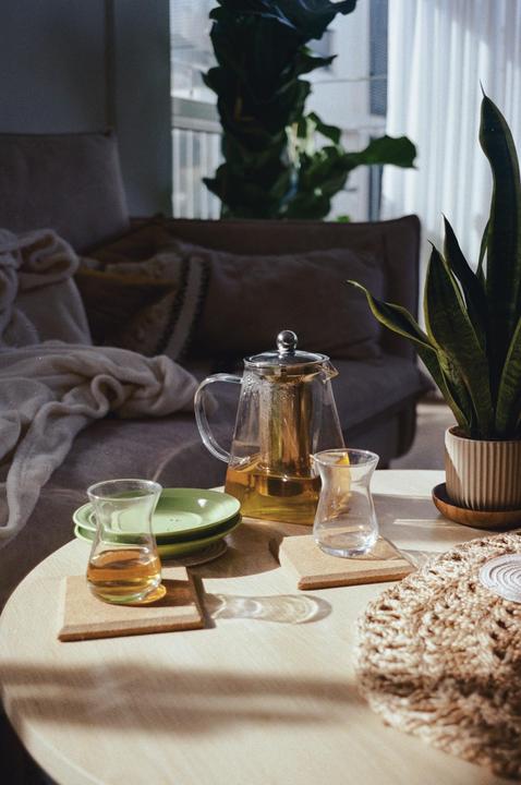 A glass teapot and two glasses of tea sit on a round wooden table in a sunlit room.