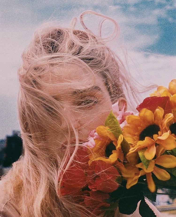 A woman with long blonde hair holds a bouquet of flowers to her face.
