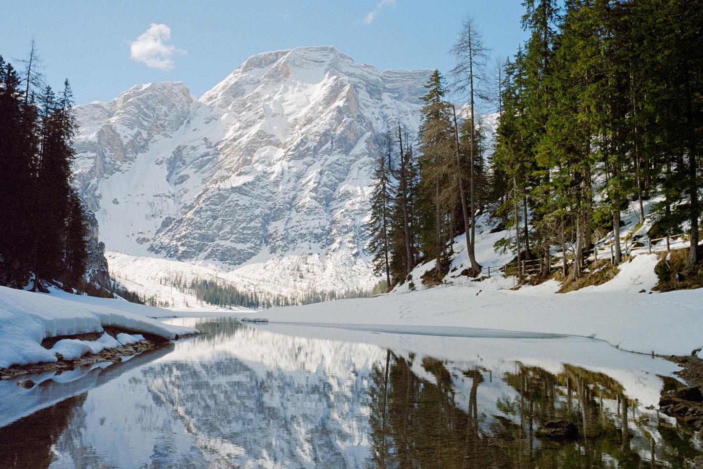 A snow-covered mountain reflects in a lake surrounded by pine trees and snow.