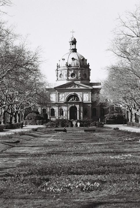 A domed building with a cross on top stands at the end of a grassy area lined with trees.