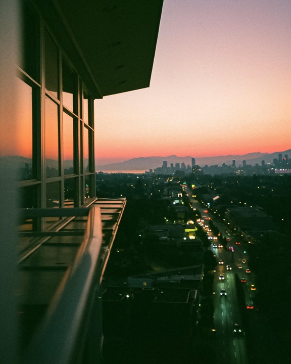 A city street with cars and buildings is visible from a high vantage point at dusk, with mountains in the distance.