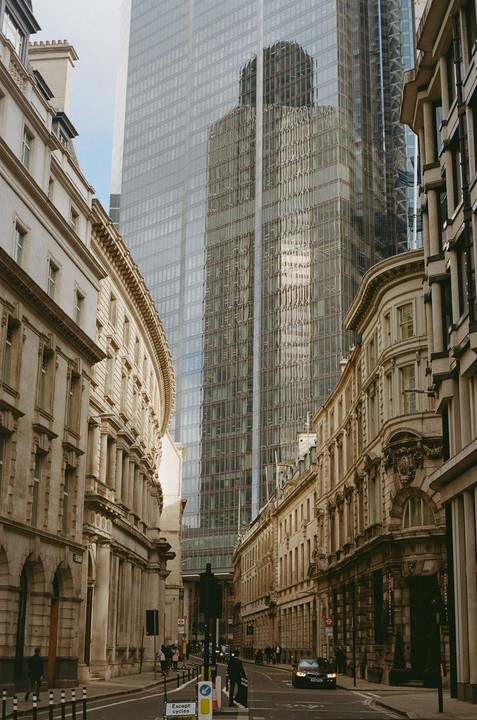 A narrow street with historic buildings on either side leads to a modern glass skyscraper in London.