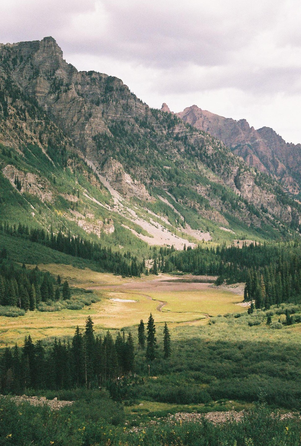 A valley with a winding stream is nestled between two large mountains covered in trees.