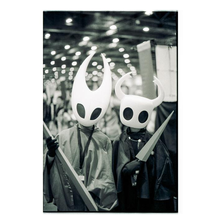 Two people in costumes with large white masks and capes stand side by side.