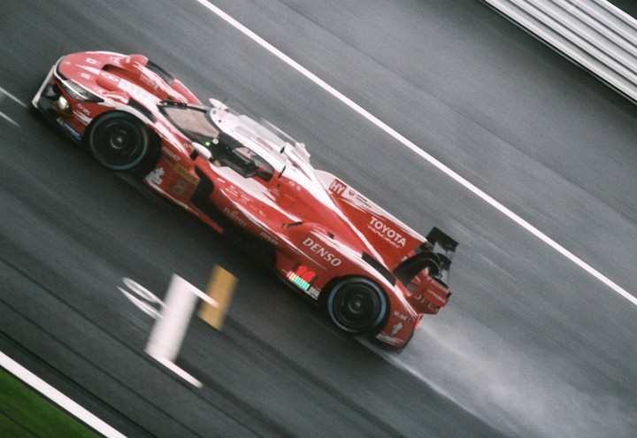 A red and white Toyota race car speeds along a wet track at Fuji Speedway.