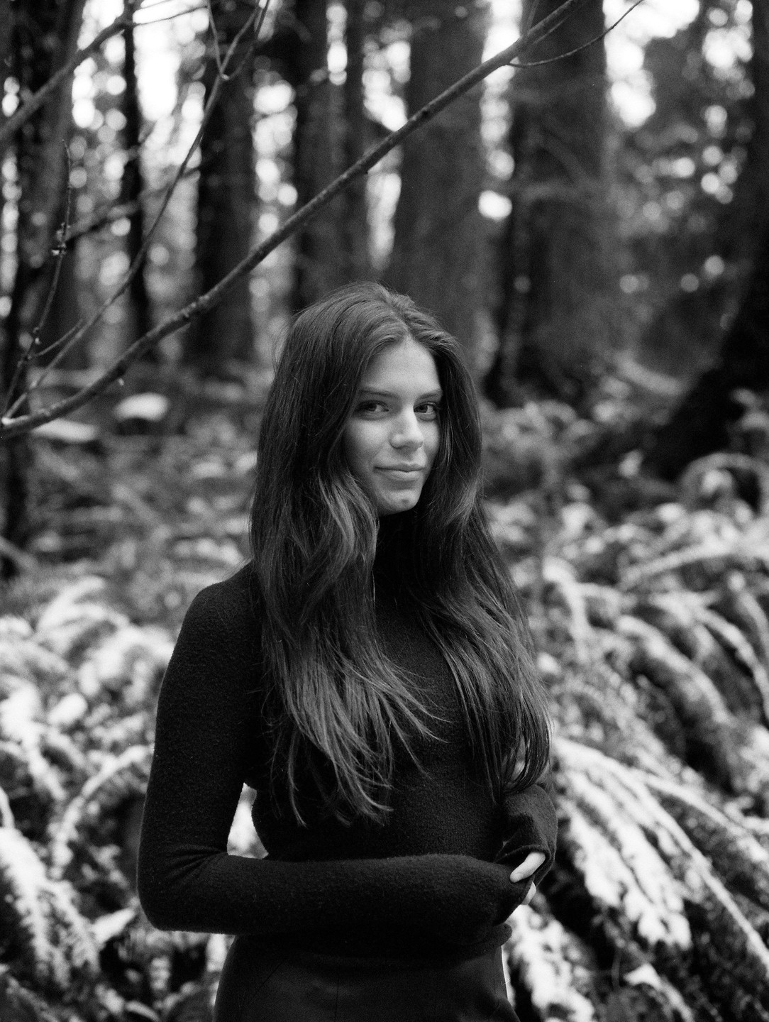 A woman with long hair stands in a forest with snow-dusted ferns.