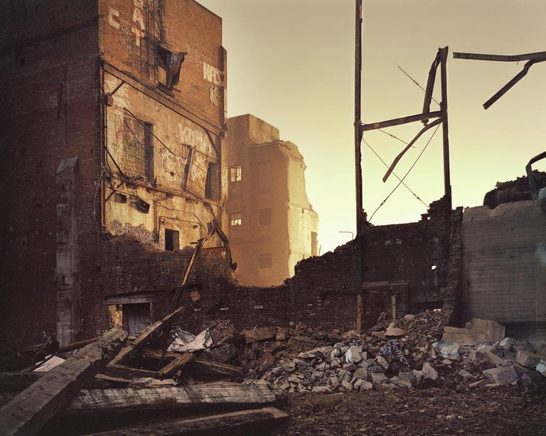 A demolished brick building stands among rubble and debris under a hazy sky.
