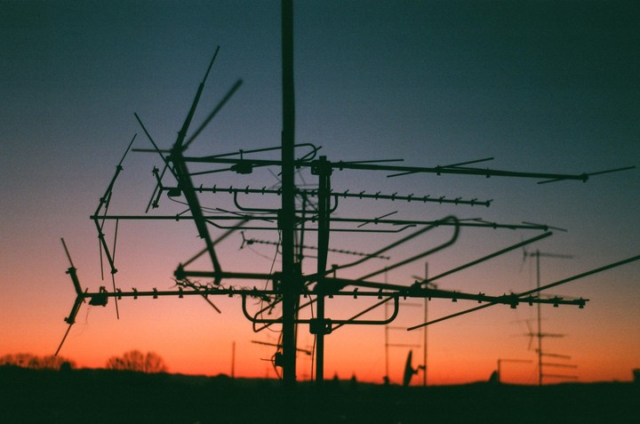 A silhouette of an antenna array stands against a vibrant sunset sky.