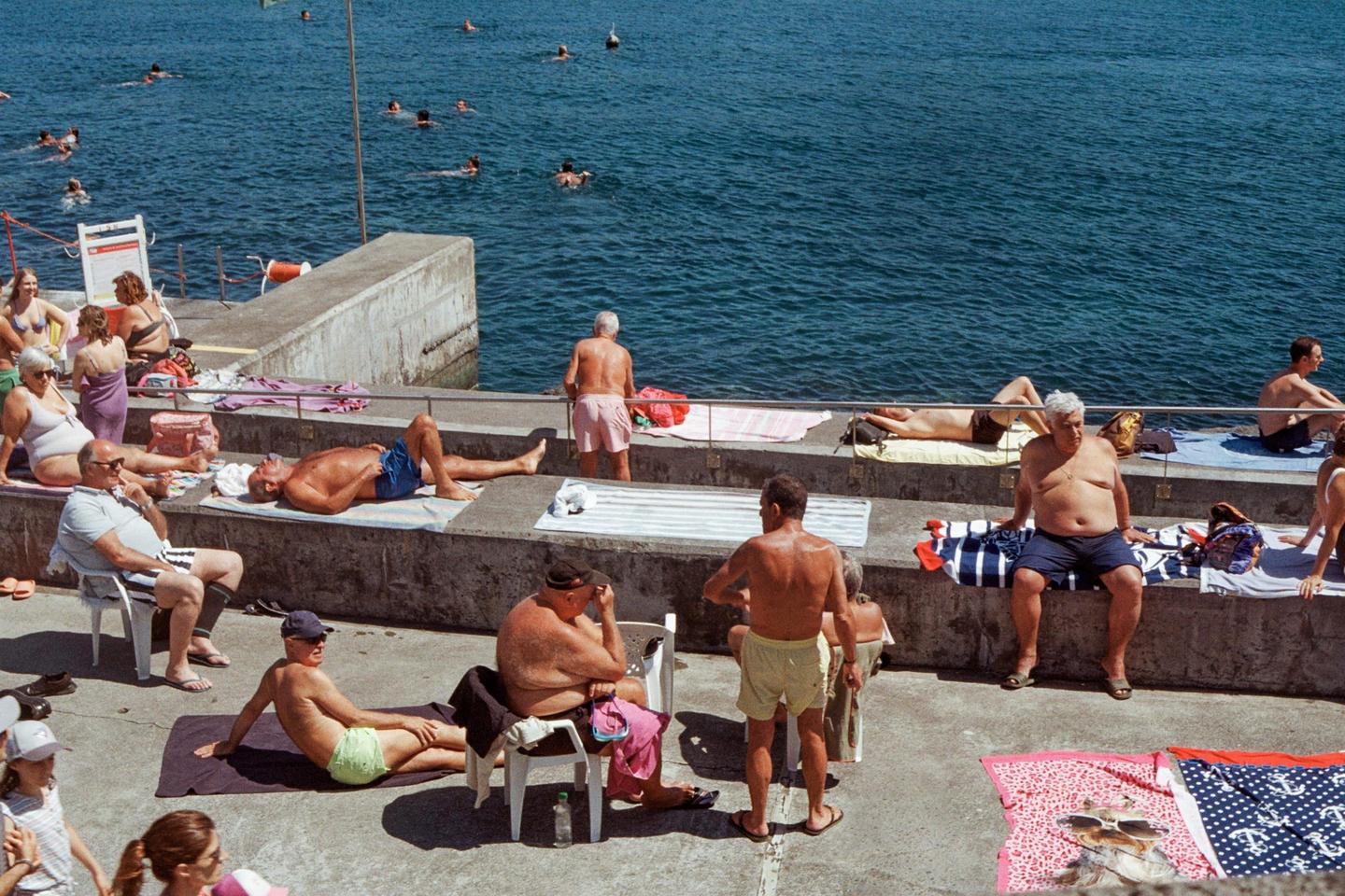Many people are sunbathing and swimming in a concrete area next to the ocean.